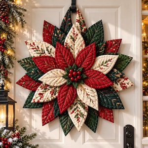 Può includere: Una ghirlanda di stella di Natale in tessuto con petali trapuntati nei toni del rosso intenso, verde scuro e crema con motivi di agrifoglio. Il centro è decorato con un grappolo di piccole bacche rosse lucide, sospesa da un occhiello in tessuto.