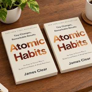 May include: Two copies of the book Atomic Habits by James Clear with off-white covers and metallic copper lettering. The text reads New York Times Bestseller, Tiny Changes, Remarkable Results, Atomic Habits, An Easy & Proven Way to Build Good Habits & Break Bad Ones, and James Clear.