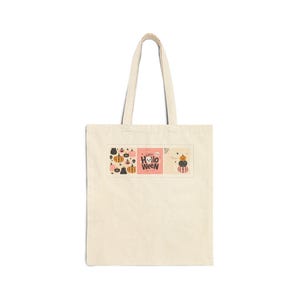 Peut inclure: Un sac fourre-tout en toile beige avec une impression graphique rectangulaire. Le motif comprend diverses illustrations de citrouilles, un panneau central rose avec le texte "HAPPY HOLLOWEEN" et un fantôme, et trois citrouilles empilées.