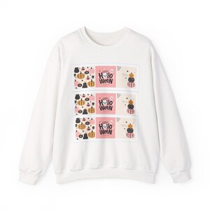 Könnte beinhalten: Ein weißes Sweatshirt mit Rundhalsausschnitt und einem wiederkehrenden Grafikdruck aus drei horizontalen Feldern. Jedes Feld zeigt ein Kürbismuster, den Text "HAPPY HOLLOWEEN" mit einem Geist und einen Stapel aus drei Kürbissen in Rosa, Schwarz und Orange.