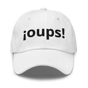 May include: A white baseball cap featuring the text ¡oups! embroidered in black thread across the front panels. The cap has a structured crown, a curved brim, and a button at the top center, providing a clean and simple design for headwear.