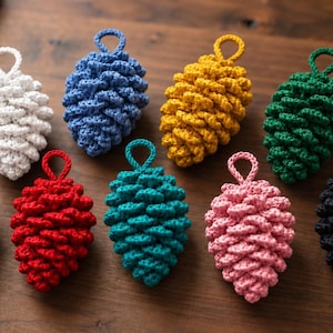 Puede incluir: Un conjunto de nueve adornos de piña hechos a ganchillo en varios colores: blanco, azul, amarillo, verde, morado, rojo, verde azulado, rosa y negro. Cada adorno presenta una superficie texturizada en capas y un pequeño lazo circular superior.