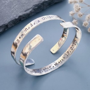 May include: A silver-toned metal cuff bracelet with a hammered texture. The outer surface is engraved with the text you made a difference, while the inner surface features the engraved date March 13, 2012 - March 13, 2020 in black lettering.