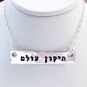 May include: Silver necklace with a hammered bar pendant inscribed with the Hebrew words "Hatikvah" and "Ul'am" which translate to "The Hope" and "Forever".