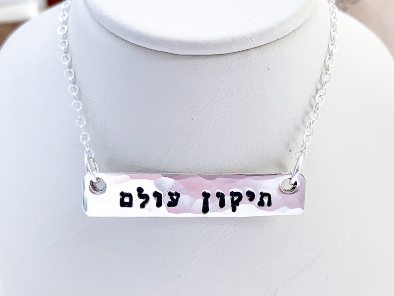 May include: Silver necklace with a hammered bar pendant inscribed with the Hebrew words "Hatikvah" and "Ul'am" which translate to "The Hope" and "Forever".
