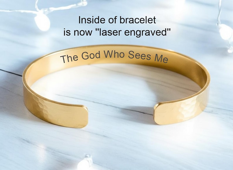 May include: Gold-coloured bracelet with the engraved text "The God Who Sees Me." The inside of the bracelet is laser engraved. The bracelet has a hammered texture and is open-ended.