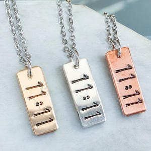 May include: Three silver necklaces with rectangular pendants that say "11:11" in a handwritten font. The pendants are silver, gold, and copper.
