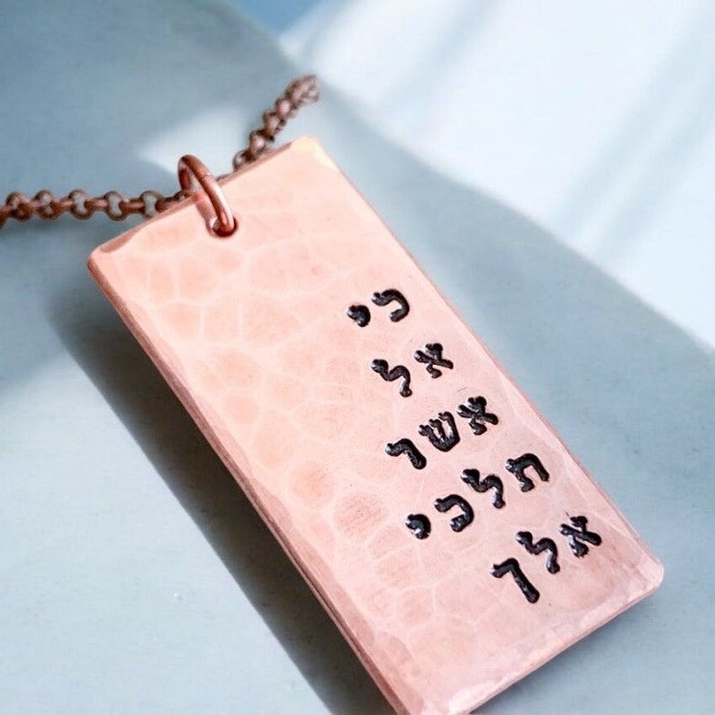 May include: A copper necklace with a rectangular pendant featuring Hebrew text. The pendant has a hammered texture.