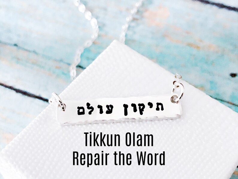May include: Silver necklace with a bar pendant that reads "Tikkun Olam" in Hebrew. The pendant is inscribed with the Hebrew words "Tikkun Olam" which translates to "Repair the World".