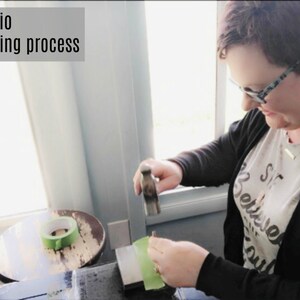 May include: A person hand stamping a piece of metal jewelry with a hammer on a green surface. The text "Jewelry Studio Hand stamping process" is visible at the top of the image.
