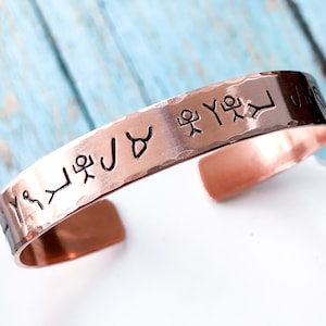May include: Copper cuff bracelet with hammered texture and etched symbols. The open cuff design allows for easy wear. The bracelet is a warm copper color and features a series of etched symbols around the band.