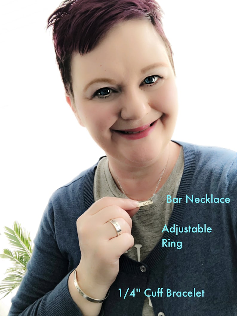 May include: A woman is wearing a blue sweater, a silver bar necklace with the word "life" engraved on it, a silver ring, and a silver 1/4 inch cuff bracelet. The necklace is labeled "Bar Necklace", the ring is labeled "Adjustable Ring", and the bracelet is labeled "1/4" Cuff Bracelet".