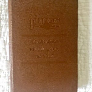 May include: A brown, rectangular, hardbound Dietzgen Engineers' Field Book No. 403F. The cover features a textured finish with the brand name, the title, and the model number embossed in the center. The book has a vertical orientation.