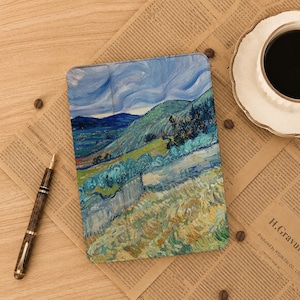 Puede incluir: Una funda rectangular para tableta con una reproducción impresa de un paisaje con cielos azules arremolinados, colinas verdes y campos dorados. La funda tiene una superficie texturizada y un diseño plegable con pinceladas gruesas y visibles.