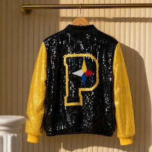 May include: A varsity-style jacket featuring a black sequined body and bright yellow sequined sleeves. The back displays a large letter P in yellow sequins, centered with a star-shaped emblem in white, yellow, red, and blue sequins.