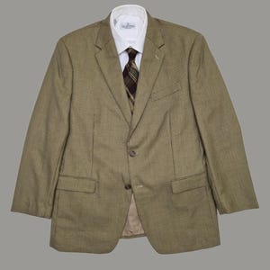 Peut inclure: Un blazer à micro-carreaux beige et marron avec un revers cranté, deux boutons sur le devant et deux poches à rabat. En dessous, une chemise blanche à col est portée avec une cravate à carreaux marron, vert et beige. L'étiquette indique Valentino.