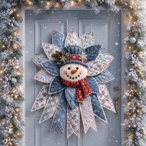 May include: A quilted fabric snowman wreath featuring a central snowman face with an orange carrot nose, wearing a blue hat and a red scarf. The wreath is constructed from layered, pointed fabric petals in shades of blue, white, and grey with snowflake and floral patterns, accented with small holly berries and silver snowflakes.