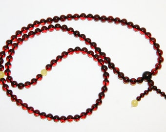 Pode incluir: Um colar de contas de mala de âmbar vermelho com uma conta preta e duas contas amarelas no final.