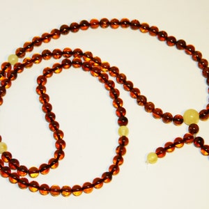 Pode incluir: Um colar longo de contas de &acirc;mbar com um tassel e algumas contas de cor amarela clara. O colar &eacute; feito de contas redondas e &eacute; enfiado em um cord&atilde;o.
