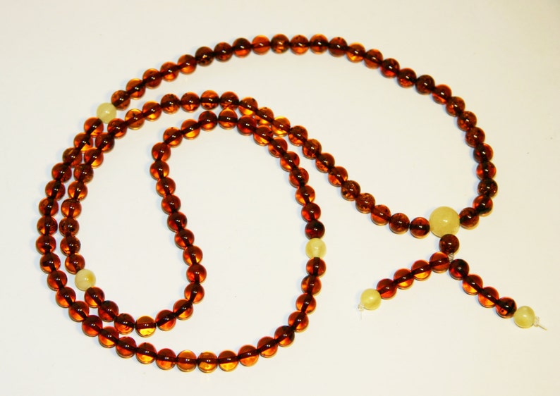 Pode incluir: Um colar longo de contas de &acirc;mbar com um tassel e algumas contas de cor amarela clara. O colar &eacute; feito de contas redondas e &eacute; enfiado em um cord&atilde;o.
