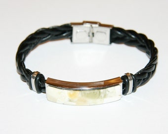 Puede incluir: Un brazalete de cuero trenzado negro con una barra de metal plateado y una incrustación de piedra blanca.