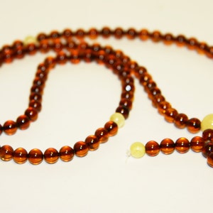 Pode incluir: Um colar de contas de mala de &acirc;mbar marrom com um tassel e duas contas brancas. O colar &eacute; feito de contas redondas e &eacute; enfiado em um cord&atilde;o.