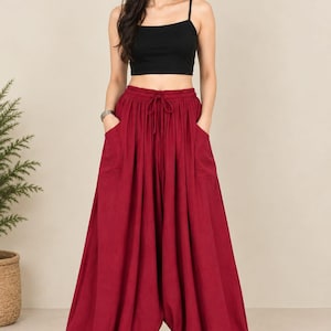 May include: A black spaghetti strap crop top paired with loose-fitting, deep red harem pants. The pants feature a gathered elastic waistband with a drawstring tie, two side pockets, and elasticized cuffs at the ankles, creating a voluminous silhouette.