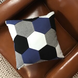 May include: A decorative pillow with a geometric pattern of hexagons in shades of gray, white, black, and blue.