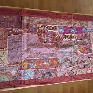 Könnte beinhalten: Ein rechteckiger Tischläufer mit einem Patchwork-Design in Violett-, Magenta- und Kastanientönen. Der Stoff ist mit aufwendigen Stickereien, Blumenmustern, kleinen runden Spiegeln und metallischen Fadenakzenten verziert.
