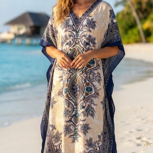 Könnte beinhalten: Ein bodenlanger Kaftan mit V-Ausschnitt und weiten Ärmeln, verziert mit einem detaillierten Paisley- und Blumenmuster in Marineblau, Creme und gedämpftem Petrol. Das Kleidungsstück hat einen einfarbigen marineblauen Saum an den Kanten.