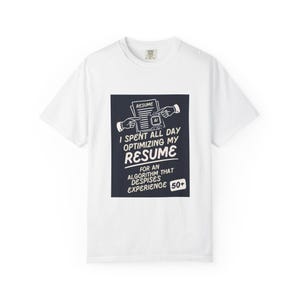 Peut inclure: Un t-shirt blanc à manches courtes avec un graphique rectangulaire sombre représentant un CV, deux mains pointant vers celui-ci, et le texte : I SPENT ALL DAY OPTIMIZING MY RESUME FOR AN ALGORITHM THAT DESPISES EXPERIENCE 50+.