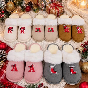 May include: Ten slip-on slippers with white faux fur trim, arranged in pairs. Colors include cream, beige, brown, pink, and gray. Each slipper features a red letter patch decorated with small Christmas-themed icons like Santa hats, stockings, or bows.