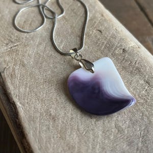May include: A silver chain necklace with a pendant. The pendant is a unique shape, with a white and purple marbled design. The pendant is attached to the chain with a silver bail.