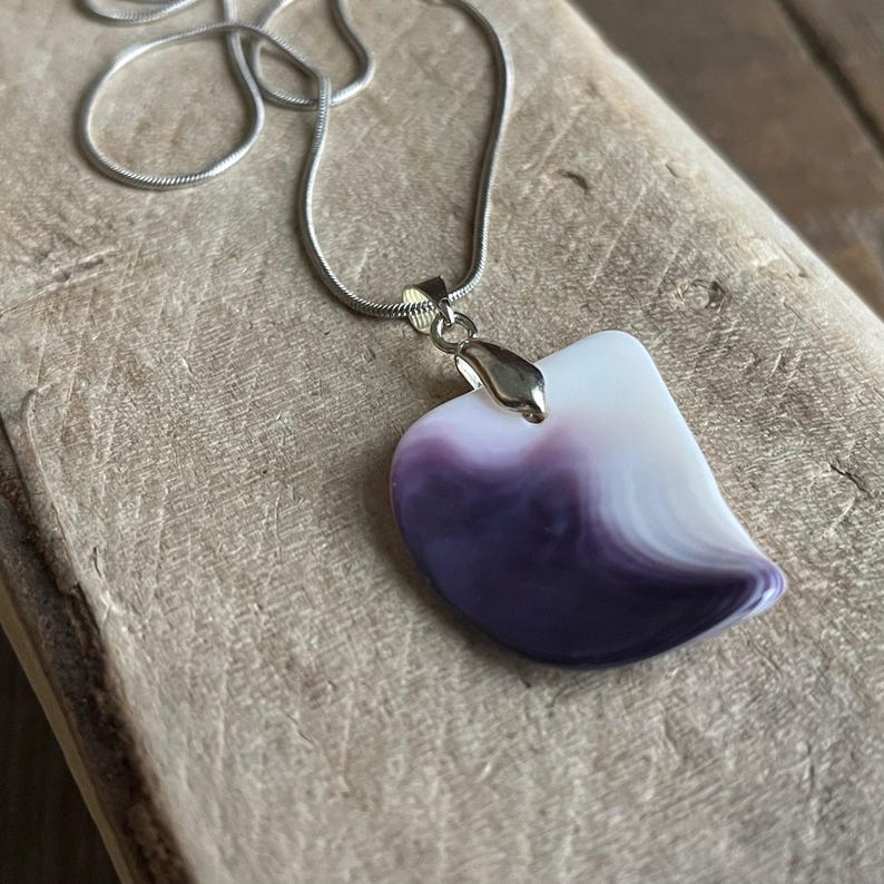 May include: A silver chain necklace with a pendant. The pendant is a unique shape, with a white and purple marbled design. The pendant is attached to the chain with a silver bail.