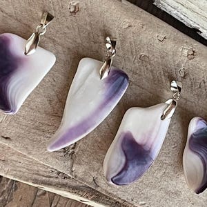 May include: Four pendants with silver-colored bails. The pendants are white with swirling purple patterns. Two are heart-shaped, and two are more abstract shapes. The pendants are displayed on a weathered wooden surface.