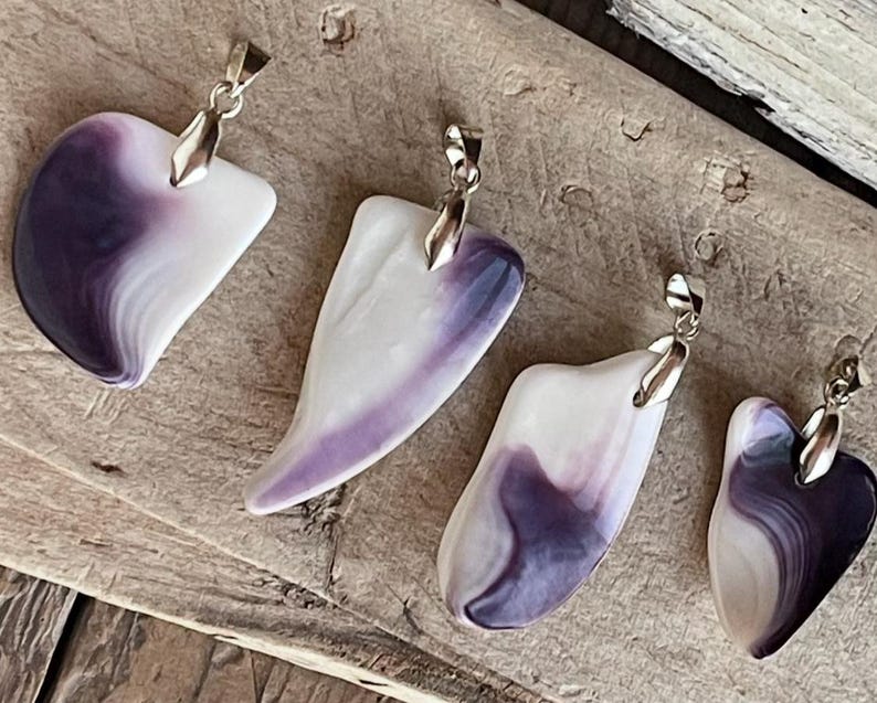 May include: Four pendants with silver-colored bails. The pendants are white with swirling purple patterns. Two are heart-shaped, and two are more abstract shapes. The pendants are displayed on a weathered wooden surface.