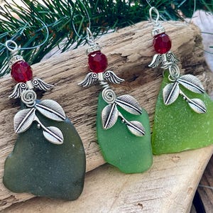 Pode incluir: Tr&ecirc;s enfeites de vidro do mar com asas de anjo prateadas e detalhes de folhas. Cada enfeite tem um tom diferente de vidro do mar verde, com uma conta vermelha no topo. Os enfeites s&atilde;o exibidos em um peda&ccedil;o de madeira flutuante.