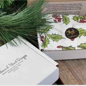 Pu&ograve; includere: Una scatola di spedizione in cartone bianco con il testo Beachwood Street Designs Handmade Just For You Fairhaven, MA 02719. All'interno, carta velina bianca presenta un motivo di foglie di agrifoglio verdi e bacche rosse, fissata da un adesivo nero.