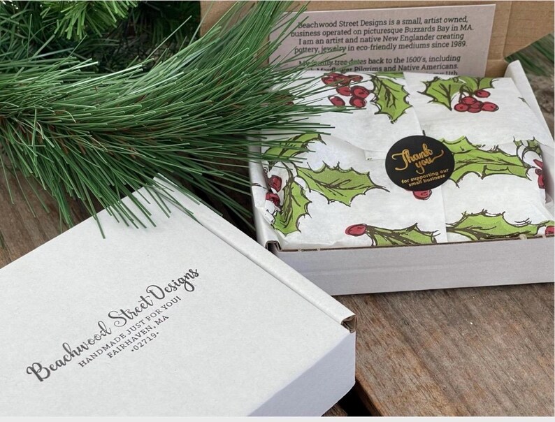 Pu&ograve; includere: Una scatola di spedizione in cartone bianco con il testo Beachwood Street Designs Handmade Just For You Fairhaven, MA 02719. All'interno, carta velina bianca presenta un motivo di foglie di agrifoglio verdi e bacche rosse, fissata da un adesivo nero.