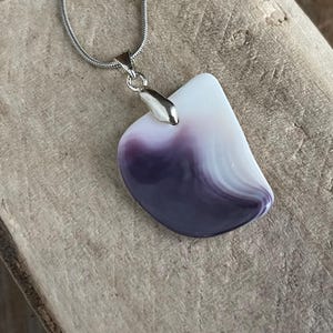 May include: A pendant necklace featuring a polished, abstract-shaped stone with a gradient of white to deep purple hues. The stone is suspended from a silver-colored chain.