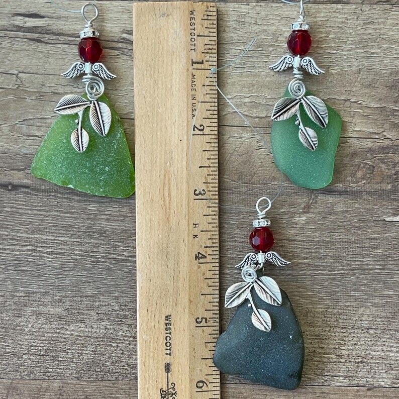 Pode incluir: Tr&ecirc;s enfeites feitos &agrave; m&atilde;o com vidro do mar, asas de anjo de metal prateado e contas vermelhas. Os peda&ccedil;os de vidro do mar s&atilde;o em v&aacute;rios tons de verde e cinza. Os enfeites t&ecirc;m cerca de 5 a 7,6 cm de comprimento.