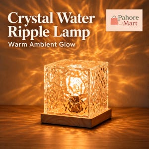 May include: A cube-shaped lamp with a textured, clear glass exterior that emits a warm, golden light, creating ripple-like patterns on surrounding surfaces. The glass cube rests on a square, light-colored wooden base.