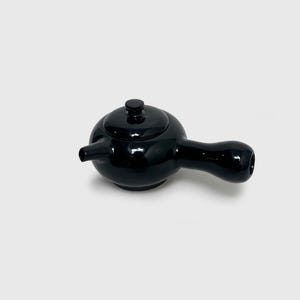 May include: A glossy black ceramic teapot featuring a rounded body, a short spout, and a side-mounted handle. The teapot includes a matching circular lid with a small knob on top. The surface has a smooth, reflective finish throughout.