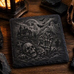 May include: A square black slate coaster featuring an engraved scene of a haunted house, a full moon, flying bats, a ghost, a skull, and a skeletal hand emerging from the ground. The design includes gravestones and a dark, textured landscape.
