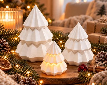 Peut inclure: Trois décorations de Noël en forme de sapin, blanches, géométriques et à facettes, avec un design angulaire à étages. Le plus petit sapin au centre émet une lumière chaude, tandis que les deux plus grands sont opaques.
