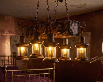 May include: A rustic chandelier featuring a dark, weathered wooden beam suspended by metal chains. Five lantern-style light fixtures with dark metal frames and clear glass panels hang from the beam, each containing a glowing light bulb.