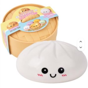 Könnte beinhalten: Ein weißes, knautschbares Dumpling-Spielzeug mit lächelndem Gesicht und rosa Wangen, begleitet von einem beigen Dampfgarer-Behälter aus Kunststoff. Die Verpackung zeigt den Text "SQUISHY DUMPLING" und "DO NOT EAT" sowie bunte Dumpling-Abbildungen.