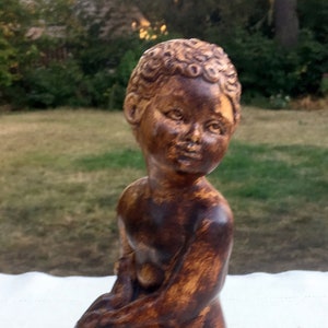 Könnte beinhalten: Eine braune Holzfigur einer Person, die kniet und die Hände gefaltet hat. Die Figur hat ein detailliertes Gesicht und lockiges Haar.