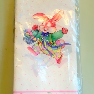Könnte beinhalten: Ein weißes Papierblatt zum Thema Ostern mit einem Cartoon-Hasen, der einen Korb mit Eiern trägt. Der Hase trägt grüne und karierte Kleidung. Das Blatt hat rosa Tupfen und einen rosa Blumenrand. Das Blatt befindet sich in einer transparenten Plastikverpackung.