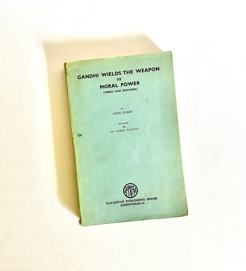 May include: A vintage book titled "GANDHI WIELDS THE WEAPON OF MORAL POWER" with a light green cover. The book includes the author's name, Gene Sharp, and a foreword by Dr. Albert Einstein. The book is from the Navajivan Publishing House, Ahmedabad-14.